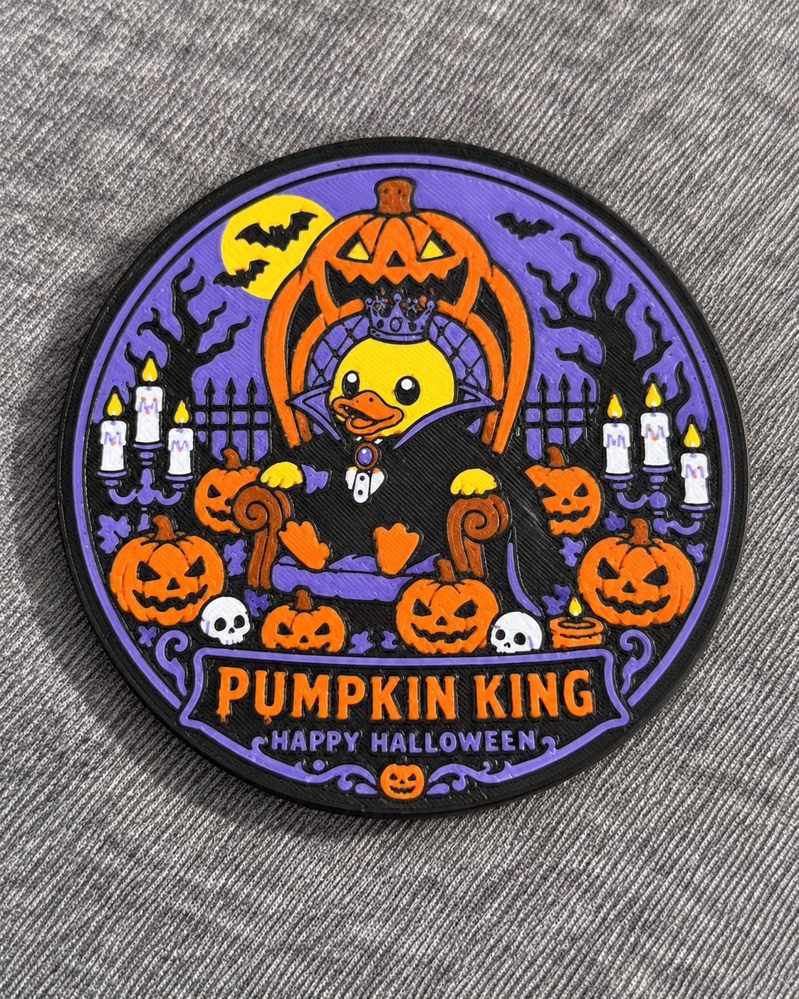 A circular coaster featuring a cartoon duck in a vampire outfit surrounded by pumpkins, candles, bats, and the text 'PUMPKIN KING HAPPY HALLOWEEN' on a gray textured fabric background.